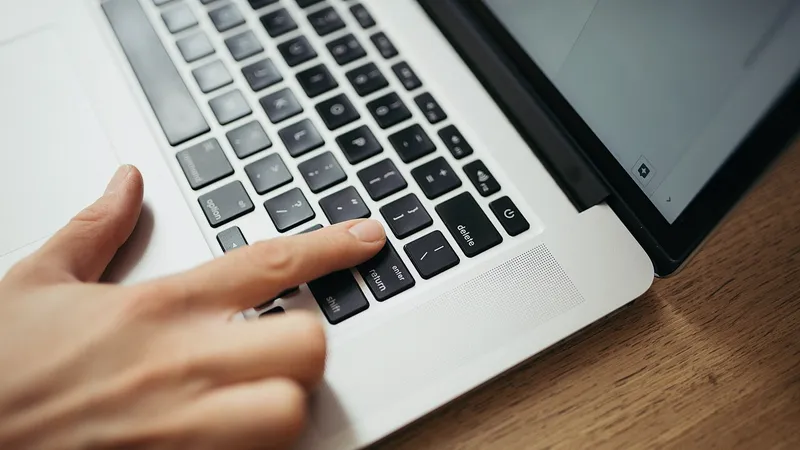 Hands writing notes in a notebook beside an open laptop
