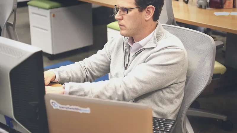 Man wearing a headset works at a computer in an open office