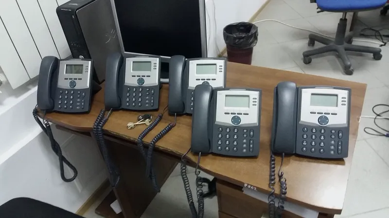Black IP desk phone on a light wooden desk