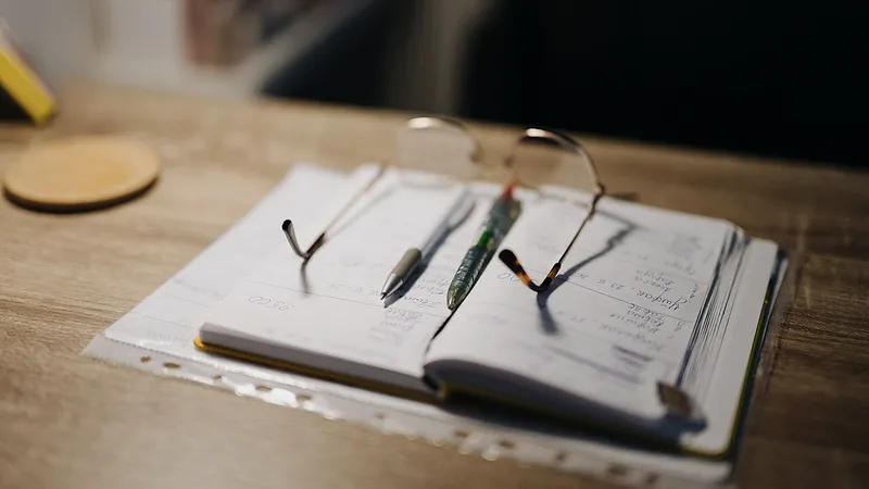 Open notebook with handwritten notes, pens and reading glasses on a desk