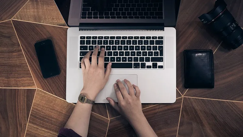 Hands on a laptop keyboard with a phone alongside