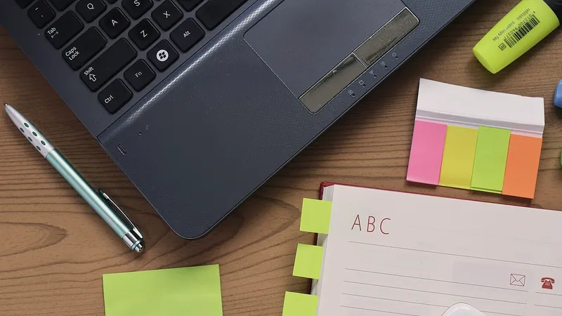 Laptop, pen, notebook and coloured sticky tabs on a wooden desk